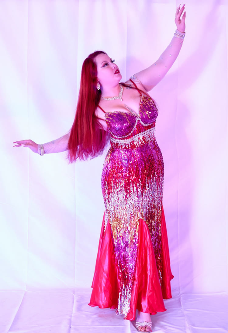 Luna Gozaine con traje de lentejuelas fucsia y rojo, brazo en alto